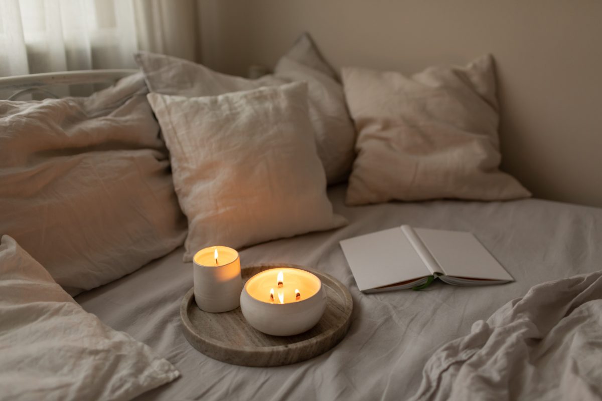 Scented Candles In Ceramic Bowls On Linen Bed With Book At Home.