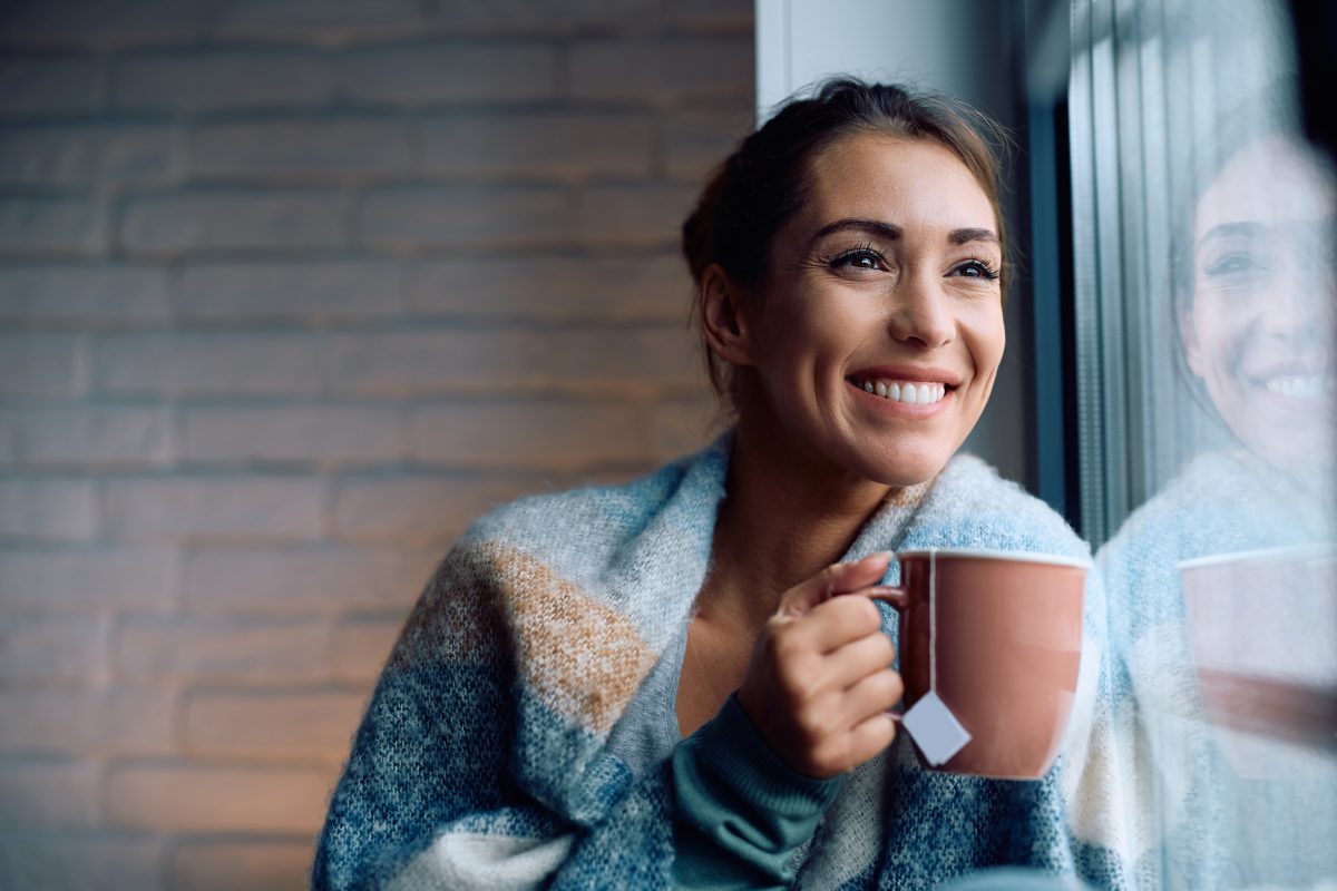 Happy Woman Enjoying Cup Of Warm Tea By The Window.