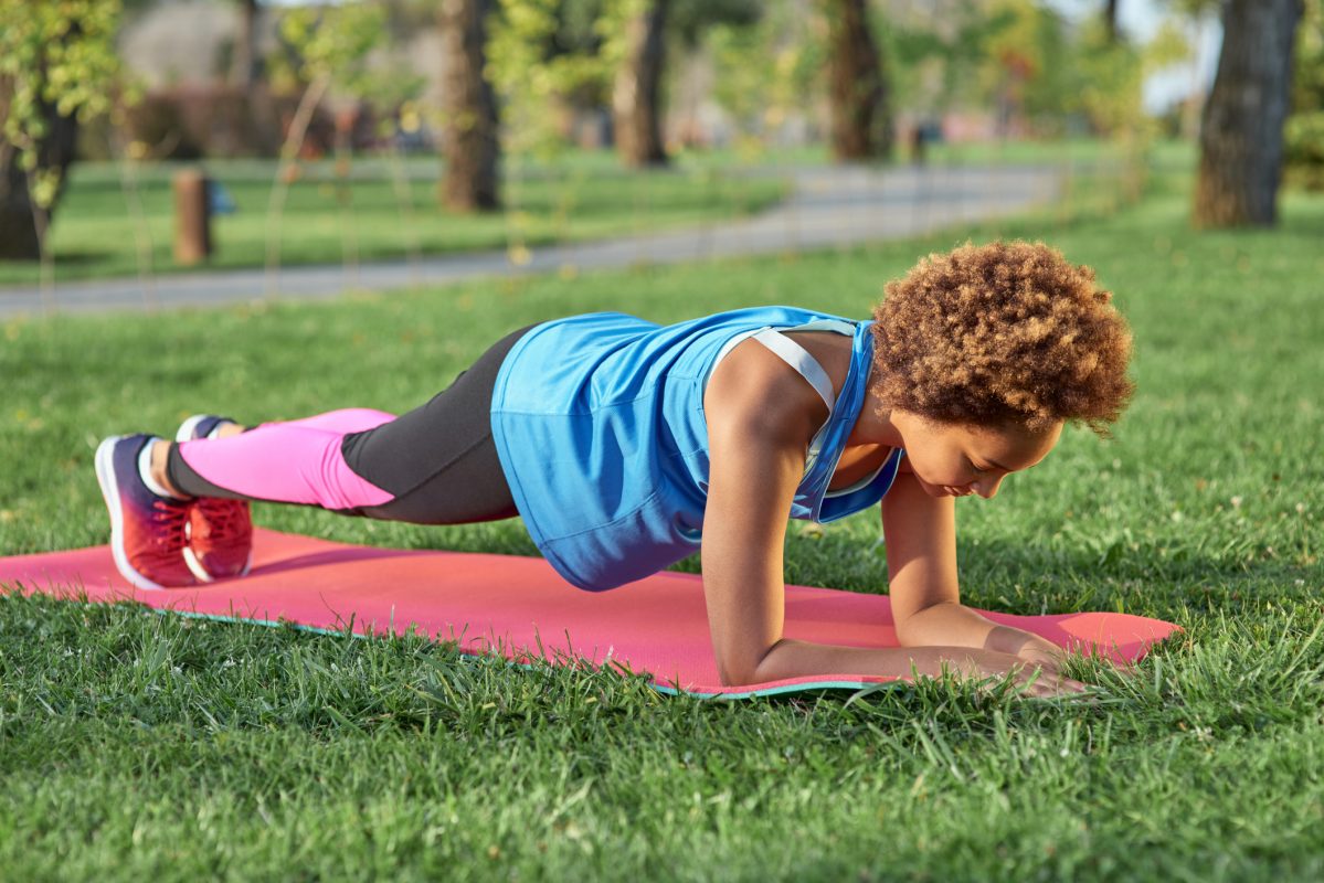 Sporty Afro American Girl Doing Plank On Yoga Mat In Park