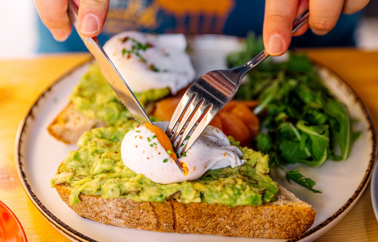 Man Eating Avocado Toast With Poached Egg And Salmon, Close Up View