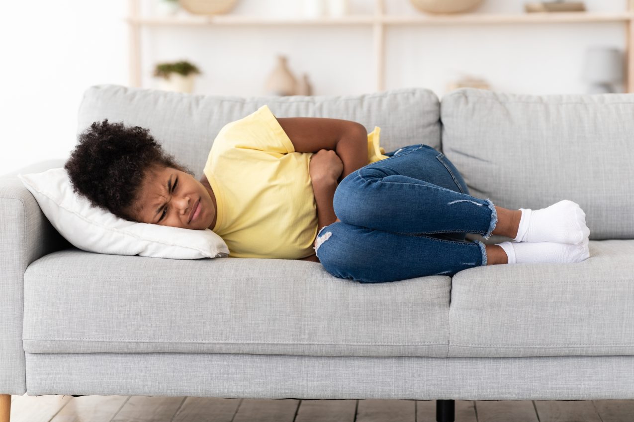 Black Girl Suffering From Abdominal Pain Lying On Sofa Indoor