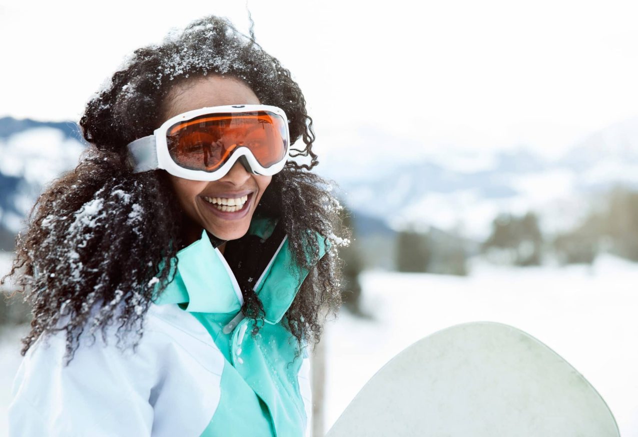 Skivakantie: portret van jonge vrouw in de sneeuw met snowboard