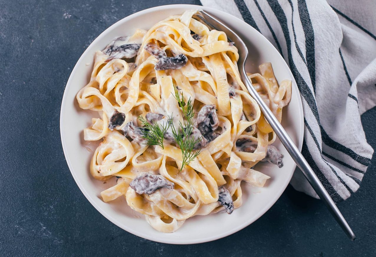 Pastagerechten Herfst: Italiaanse pasta fettuccine in een romige saus met champignon op een bord, bovenaanzicht