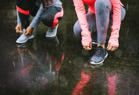 Schoenendroger: Close-up van twee vrouwen die schoenen veteren en zich klaarmaken voor een hardlooptraining in de regen.