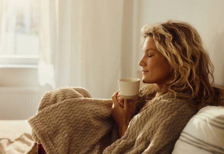 Plaid: jonge vrouw met mok koffiue in haar handen en een plaid om haar heen gewikkeld